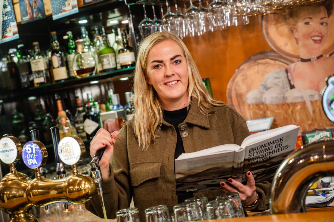 Kvinde står i bar med bog i hånden